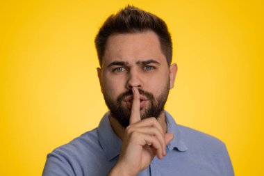 Sessiz olun lütfen. Genç beyaz adam işaret parmağını dudaklarına bastırıyor sessiz jest işareti yapıyor. Gizli saklı konuşmayın, dedikoduyu durdurun. Sarışın sakallı adam, sarı stüdyo duvarında tek başına.