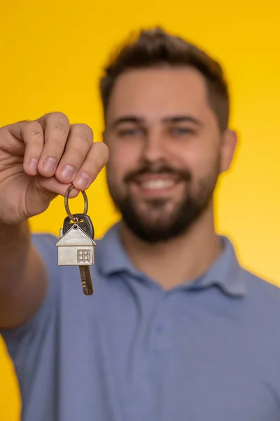 幸せな若い男の不動産業者は 賃貸物件 住宅ローンを購入し 新しい家のアパートの鍵を示す手を持ち上げる 黄色のスタジオの背景に孤立したハンサムな男 — ストック写真