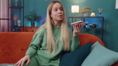 Mutlu heyecanlı kadın arkadaşlarıyla çevrimiçi telefon görüşmesi yapıyor. Mobil hoparlörlerden hoşlanan beyaz bir kızın portresi. Oturma odasında kanepede sohbet ediyorlar.