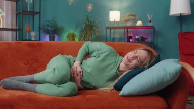 Adet sancısı çeken hasta bir kadın. Oturma odasındaki kanepede yatarken karın ağrısı çekiyor. Karnını tutan bir kız, karın ağrısı ya da regl ağrısı çekiyor. Karın ağrısı, mide iltihabı, ishal, hazımsızlık.