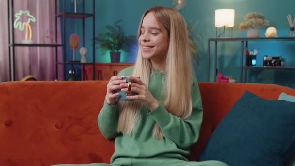 一个微笑的女人早上喝一杯热咖啡或草药茶的画像 白种人少女在沙发上的公寓客厅里独自休息 享受着舒适的放松 — 图库视频影像