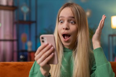 Aman Tanrım. Vay canına. Heyecanlı genç kadın akıllı telefon daktilo kullanıyor kutlama başarısı, piyango hedefi başarısı, iyi haber, zafer. Beyaz kız cep telefonunu sınıfında tutuyor.