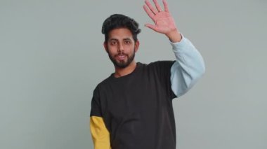 Buraya gel, bize katıl. Hoş geldiniz. Hindu sakallı adam elleriyle davetkar bir jest yapıyor, katılmak istiyor, gelmek için işaret ediyor, merhaba diyor, elveda. Gri stüdyo arka planında izole edilmiş yakışıklı Hintli adam.