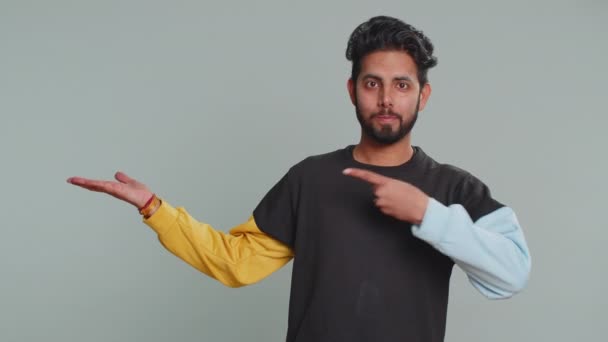 幸せな若いインド人男性が親指を表示し 空の場所を指して 商業テキストの碑文 商品の宣伝バナーのコピースペースの広告エリア ヒンズー教の男は灰色のスタジオの背景に隔離 — ストック動画