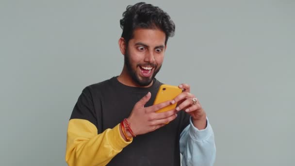 黒のセーターで幸せな興奮したインドの男は スマートフォンの入力の叫びを使用していますすごいはい大きな勝利 良いニュース 宝くじの目標達成者を発見したと言う 成功を祝う 勝利ゲーム — ストック動画