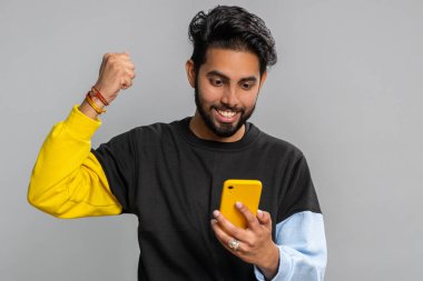 Mutlu, heyecanlı, siyah kazaklı Hintli adam akıllı telefon yazıcı kullanıyor. 