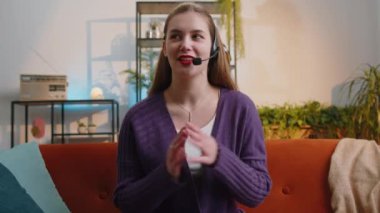 Tebessüm eden, kulaklık takan genç bir kadın, serbest çalışan, çağrı merkezi ya da destek operatörü yardım hattı, müşteri ya da iş arkadaşıyla konuşması, iletişim desteği. Kanepede oturan kız.