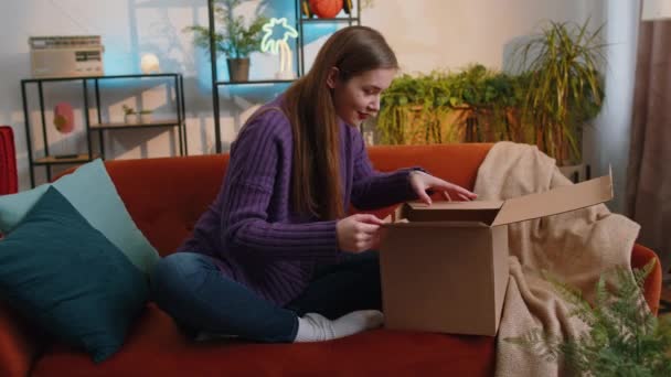 快乐的年轻女子坐在沙发上的家里公寓里打开包裹 微笑满意的女购物者网上商店顾客打开纸板箱接受快速邮寄的购物礼物 — 图库视频影像