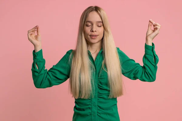 stock image Keep calm down, relax, inner balance. Young caucasian woman breathes deeply with mudra gesture, eyes closed, meditating with concentrated thoughts, peaceful mind. Girl isolated on pink background