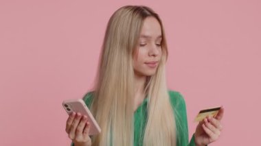 Para transferi, online alışveriş, ödeme yaparken kredi kartı ve akıllı telefon kullanan samimi beyaz kadın müşteriler. Finans ve internet. Mutlu kız pembe arka planda tek başına.