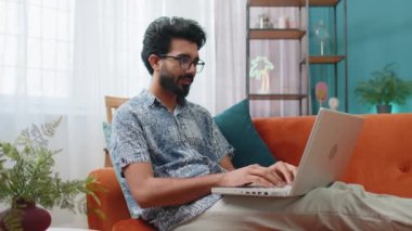 Laptop bilgisayarı kullanan Hintli bir adam, posta yoluyla iyi haber mesajı alıyor, piyango galibiyetini kutluyor piyango ikramiyesini kutluyor, evdeki dairede kanepenin üzerinde alışveriş yapıyor. Yaşam Tarzları