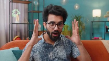 Aman Tanrım, vay canına. Genç Hintli adam kameraya büyük gözlerle bakarken şaşırdı. Ani bir zafer, iyi bir galibiyet haberi, kutlama. Evdeki kanepede oturan heyecanlı Hintli adamın portresi.