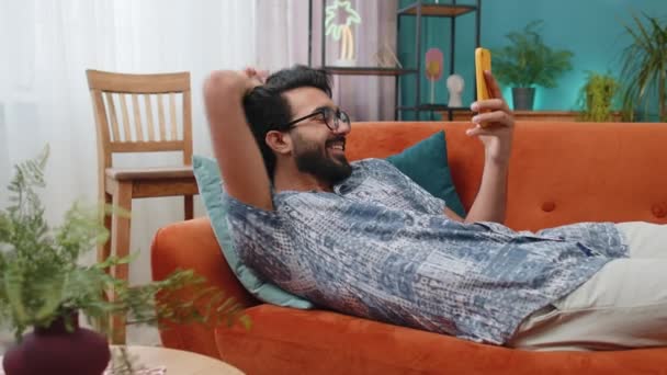 Indián Ležící Gauči Používá Mobilní Telefon Úsměvy Doma Obývací Pokoj — Stock video