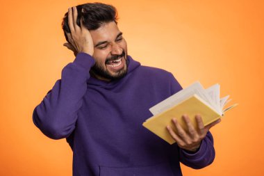 Mutlu Hintli adam komik bir masal kitabı okuyor, boş zaman hobisi, bilgelik, eğitim, öğrenme, çalışma, vay be. Yakışıklı Hintli adam turuncu stüdyo arka planında tek başına.