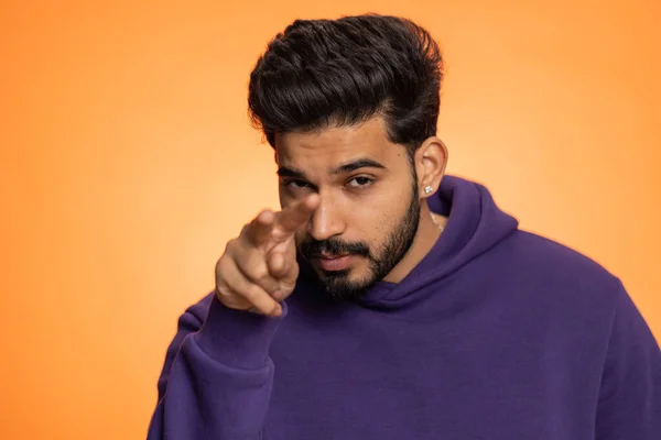 I am watching you. Young confident indian man pointing at his eyes and camera, show I am watching you gesture, spying on someone. Handsome bearded hindu guy isolated alone on orange studio background