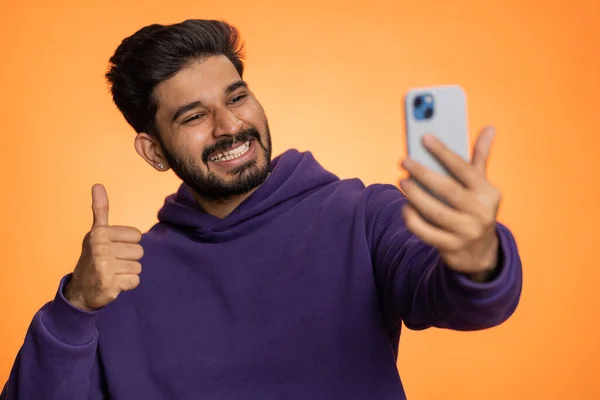 印度男子旅行博客 在智能手机上自拍 与家人或朋友在网上进行视频通话 现场翻译流 后面那个英俊的家伙在橙色背景下被隔离在室内 — 图库照片