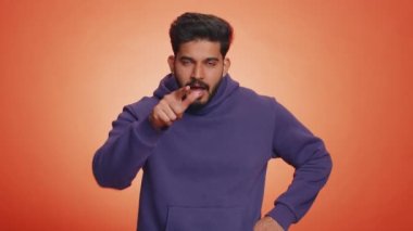 Kızgın genç Hintli bir adam parmaklarıyla bıçağı taklit ederek boğazı kestiğini gösteriyor. Saldırgan yakışıklı Hindu adam uyarı işareti gösteriyor. El boynu kesilmiş. Turuncu stüdyo arka planında kapalı.