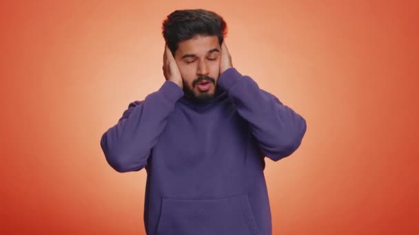 聞き耳を立てたくない いらいらするインド人の男性は 不快な騒音の大きな声を無視する助言を避けるために いいえジェスチャーをカバーするいらいらしました Handsome Hindu Guy Alone Orange Background — ストック動画