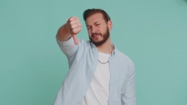 Hoşlanmamak. Tişörtlü mutsuz Lübnanlı adam işaret dilini gösteriyor, hoşnutsuzluğunu, memnuniyetsizliğini, hoşnutsuzluğunu ifade ediyor. Yakışıklı bir genç. Mavi arka planda çekilen kapalı stüdyo.