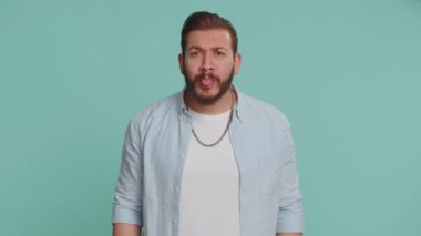 Komik, komik, genç Lübnanlı bir adam şakacı, aptal yüz ifadeleri yapıyor, suratını buruşturuyor, aylak aylak dolanıyor, dil gösteriyor. Stüdyonun mavi arka planında izole edilmiş yakışıklı, çılgın Arap adam.