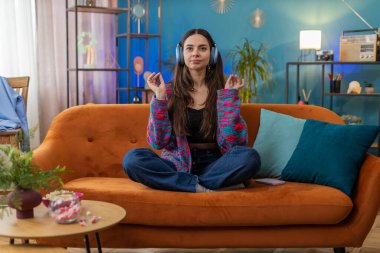 Sakin ol, rahatla, iç denge. Genç kadın derin nefes alıyor Mudra jesti ile, gözleri kapalı meditasyon yapıyor konsantre düşüncelerle, huzurlu zihinle. Evdeki kanepede oturan kızın portresi.