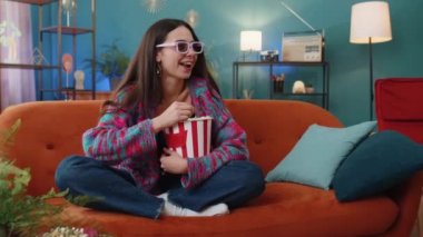 Üç boyutlu gözlüklü heyecanlı genç kadın kanepede oturup patlamış mısır yiyor ve evdeki sosyal medya içeriğindeki ilginç TV dizisi spor oyunu videosunu izliyor. Kız eğleniyor