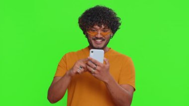 Happy excited joyful indian man in green shirt use smartphone typing browsing shouting say wow yes found out great big win, good news, lottery goal achievemen, celebrating success, winning game