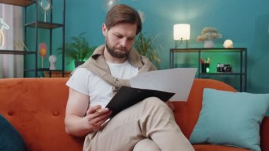 Beyaz adam evdeki koltukta belgelerle çalışıyor, bilgi okuyor, iş evrakları dizüstü bilgisayarda mali rapor hazırlıyor. Genç muhasebeci grafik belgelerini analiz ediyor, vergileri hesaplıyor.