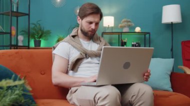 Laptop bilgisayar kullanan beyaz bir adam, posta yoluyla iyi haber mesajı alıyor, piyango galibiyetini kutluyor piyango ikramiyesi kazanılmasını kutluyor evdeki evdeki dairede kanepenin üstünde alışveriş yapıyor. Yaşam Tarzları