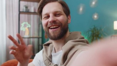 Beyaz adam blogcusunun POV 'u akıllı telefondan selfie çekiyor, sosyal medya takipçileriyle çevrimiçi video görüşmeleri yapıyor, vlog hikayeleri kaydediyor. Evdeki kanepede oturan genç adam.