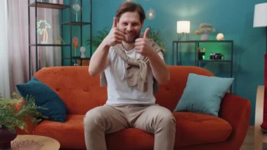 Gibi. Mutlu, heyecanlı, beyaz bir adam kameraya bakıp olumlu bir şey işaret ediyor. İyi haber, olumlu geri bildirim gibi. Oturma odasındaki kanepede oturan genç adam.