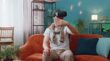 Sanal gerçeklik teknolojisi VR uygulama kulaklığı kullanarak 3D video oyunu simülasyonu izlemek için heyecanlı bir adam. Modern ev dairesindeki kanepede gözlüklü bir adamın portresi.