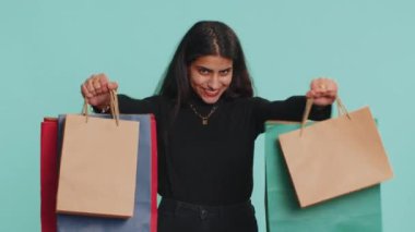Alışveriş torbaları, reklam indirimleri gösteren genç Hintli kadın. Düşük fiyatlarla gülümseyen, Kara Cuma tatillerinde alışveriş yapan. Alışveriş delisi Hindu kız stüdyo mavi arka planda izole edilmiş.