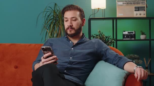 Homem Libanês Sentado Sofá Usa Sorrisos Telefone Celular Casa Sala — Vídeo de Stock