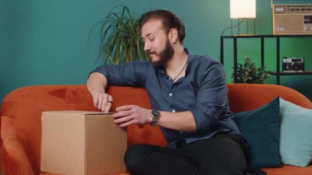 幸せなレバノン人の男宅配便の小包を自宅のアパートに座ってアンパック 笑顔満足アラビア人男買い物客オンラインショップ顧客オープン段ボール箱受信購入ギフトによる高速郵便配送 — ストック動画