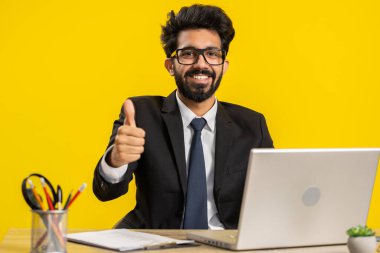Like. Happy young indian businessman guy working on laptop looking approvingly at camera showing thumbs up, like sign positive something good, positive feedback at office workplace. Freelancer man