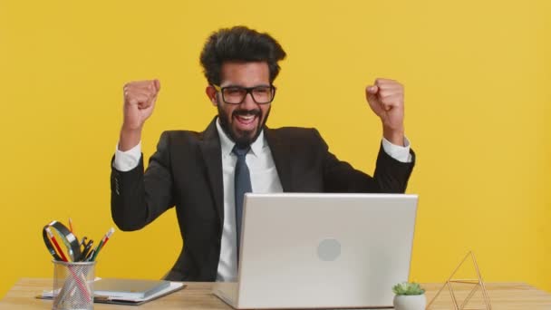 オフィスのデスクでラップトップで働いているインドのビジネスマンがブラウジングを入力すると すごいはい 素晴らしい宝くじ大当たり 良い仕事のニュース お祝いを発見したと言います フリーランスのアラブ人男性黄色の背景に隔離された — ストック動画