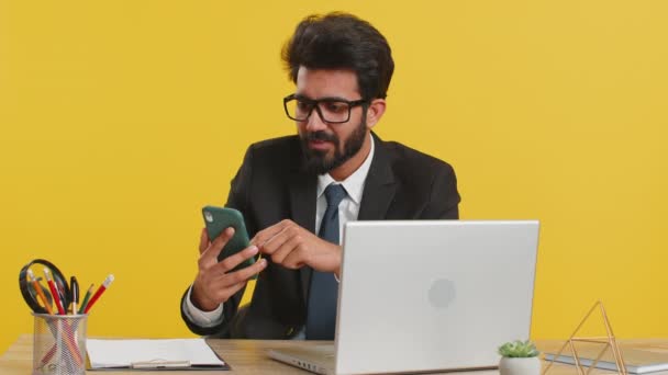 宝くじのジャックポットを獲得した突然の勝利ゲームにショックを受けたスマートフォンで働く幸せなインドのビジネスマンは良いキャリアのニュースを達成しました 黄色の背景のオフィスで興奮しました — ストック動画