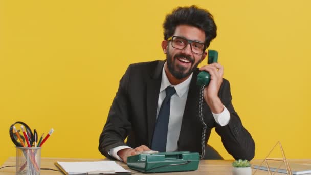 私に電話してください オフィスの職場で80年代の有線レトロヴィンテージ電話で話すインドのビジネスマン ヒンドゥ教徒の正式な訴訟 黄色の背景にラップトップ上で働くリモート遠くのオンライン — ストック動画