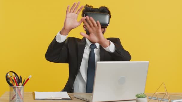 ヘッドセットヘルメットアプリを使用して刺激的なインドのビジネスマンは オフィスの職場の机でシミュレーションゲームをプレイする 仮想現実3D 360ビデオを見る ヒンズー教の男で現代的なVrゴーグル作業上の黄色の背景 — ストック動画