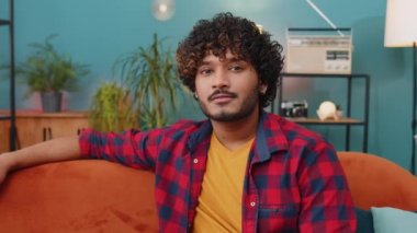 Portrait of happy calm indian man at home couch smiling friendly, glad expression looking away dreaming resting, relaxation feel satisfied concept good news, celebrate win. Hindu guy in living room