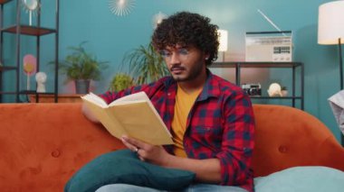 Genç Hintli adam ilginç kitapları gevşetiyor, sayfaları çeviriyor edebiyatın tadını çıkarıyor, rahat koltukta dinleniyor. Evdeki kanepede oturan mutlu Hintli adamın portresi.