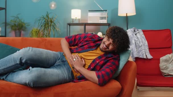 若いインド人男性ソファの上に横たわる突然の強い腹痛 胃炎の問題を感じている 自宅のアパートで症状中毒下痢消化性消化性潰瘍性膵炎を持つヒンドゥ教徒の男 — ストック動画