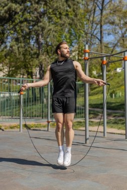 Spor giyimli atletik Lübnanlı adam ip atlıyor. Orta Doğu 'lu genç bir adam oyun alanında atlama egzersizi yapıyor. Spor tatbikatı, spor rutini, egzersiz. Güç motivasyonu. Açık havada.