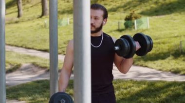 Spor kıyafetli atletik Lübnanlı adam kol ağırlığı kaldırıyor, halter egzersizleri yapıyor, kol kaslarını şişiriyor. Çocuk parkındaki genç adam. Spor, sağlık, spor, egzersiz. Kuvvet motivasyonu