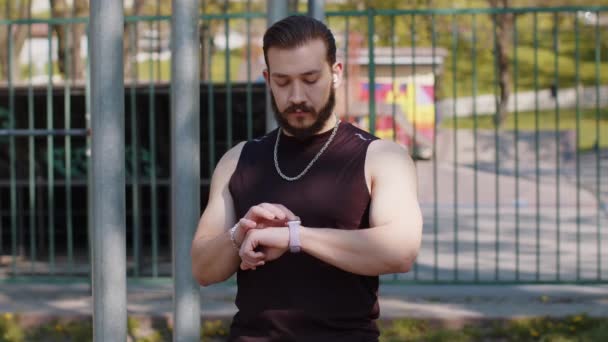 Sportowy Libańczyk Sportowej Odzieży Używający Inteligentnego Zegarka Słuchający Muzyki Słuchawkach — Wideo stockowe