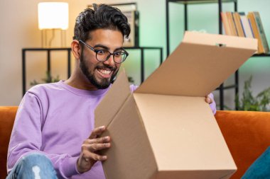Evde oturan mutlu Hintli adam teslimat paketini açıyor. Gülümseyen Hintli adam alışverişi, çevrimiçi dükkan müşterisi karton kutu açıyor hızlı posta yoluyla hediye alıyor.