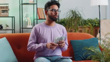 Planlama bütçesi. Zengin mutlu Hintli adam nakit sayıyor akıllı telefon hesap makinesi uygulaması kullanıyor evde faturaları hesaplıyor. Hintli adam gelir elde ediyor, kazanıyor, tatil için para biriktiriyor.