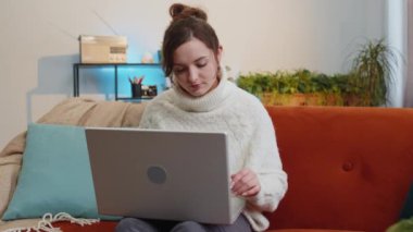 Woman freelancer opens laptop, starts working education on notebook, sends messages, makes online purchases, watching movies at home living room apartment. Portrait of girl sitting on couch. Lifestyle