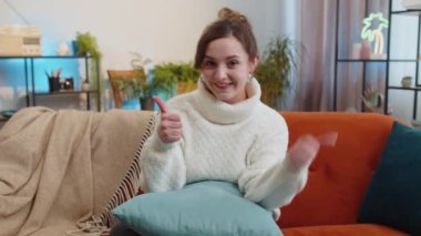 Gibi. Mutlu heyecanlı kadın kameraya onaylayıcı bir şekilde bakıyor, olumlu bir şey gösteriyor, iyi haber, olumlu geri bildirim gibi. Oturma odasındaki kanepede oturan genç kızın portresi.